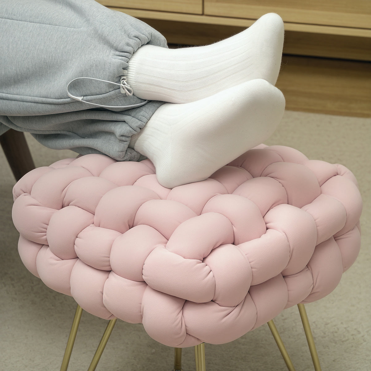 Pink woven footstool supporting a person's feet on its cushioned top