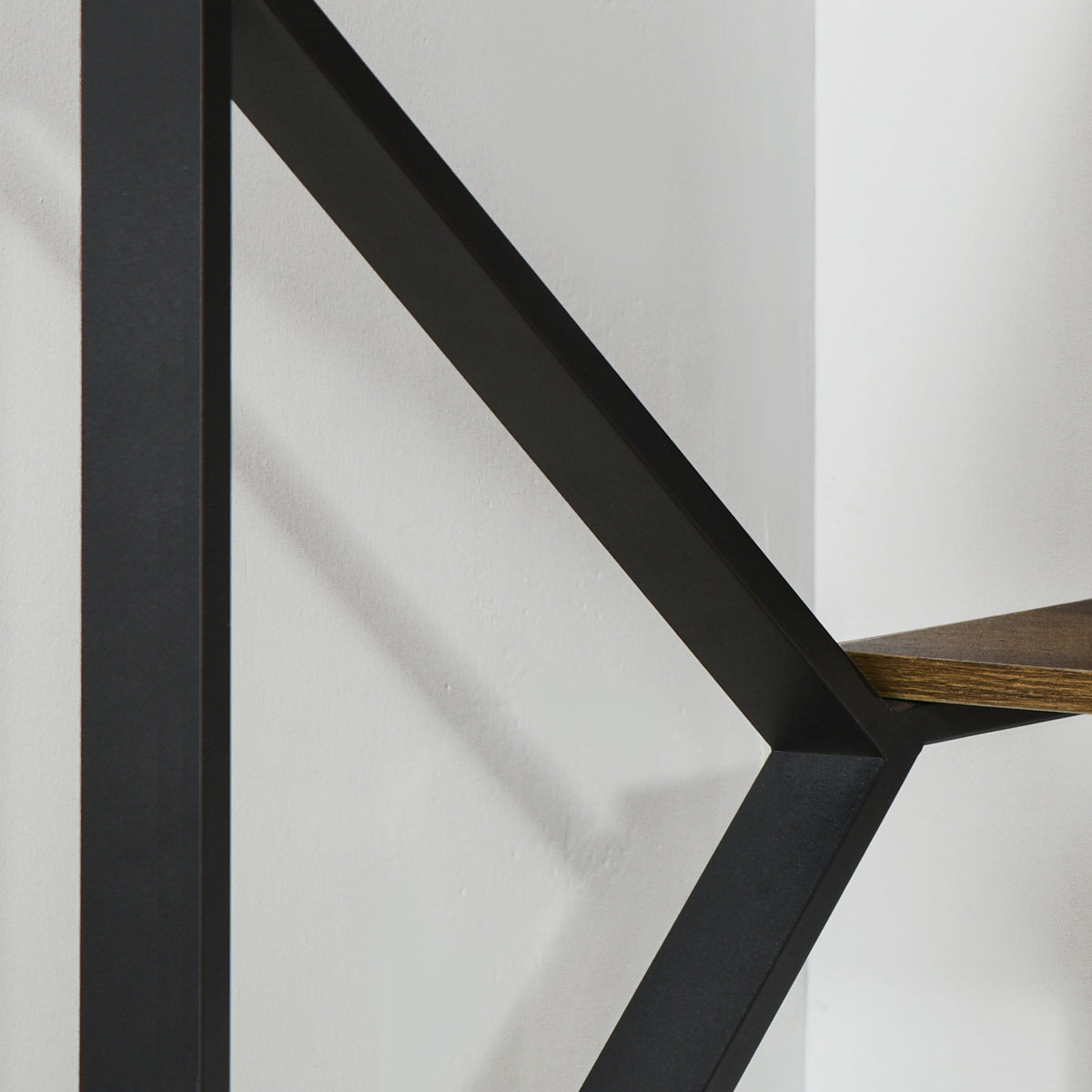 Close-up of the desk's black metal frame and brown wood-effect shelf