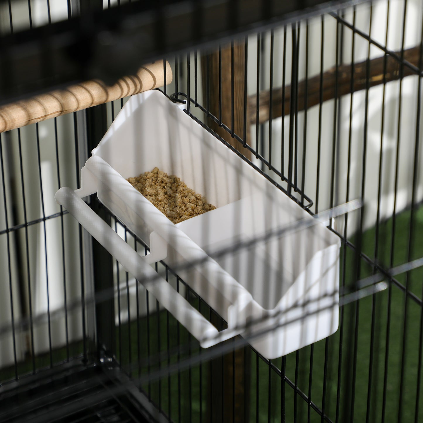 White hanging bird feeder filled with seed inside a black wire cage.