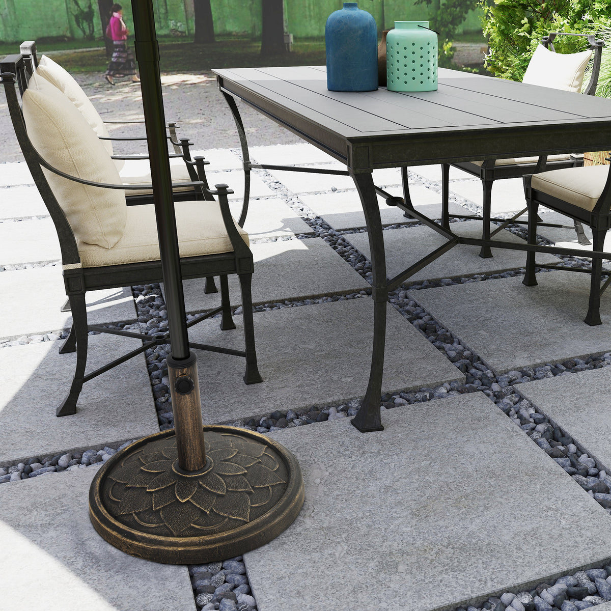 Bronze-tone flower-patterned parasol base holding an umbrella beside a patio dining set