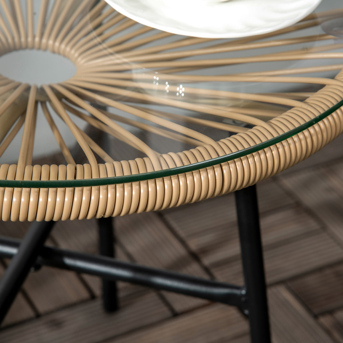 Close-up of the side table's clear glass top, woven rattan rim, and black metal frame