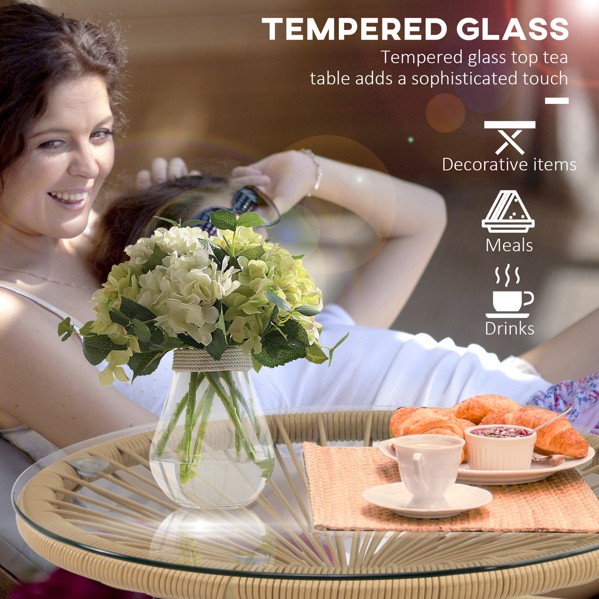 Round rattan side table with glass top, shown holding flowers, food, and drinks