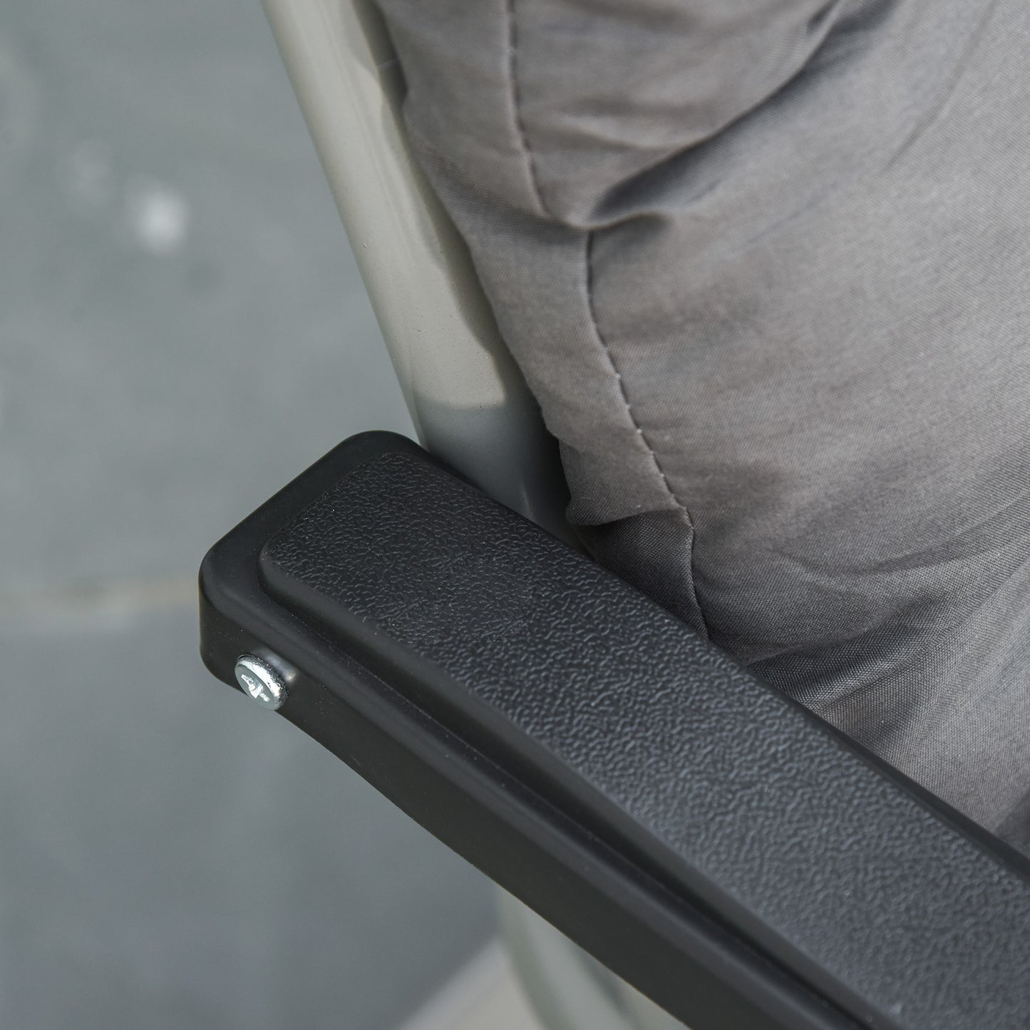 Close-up of a black textured armrest beside the gray padded lounger seat