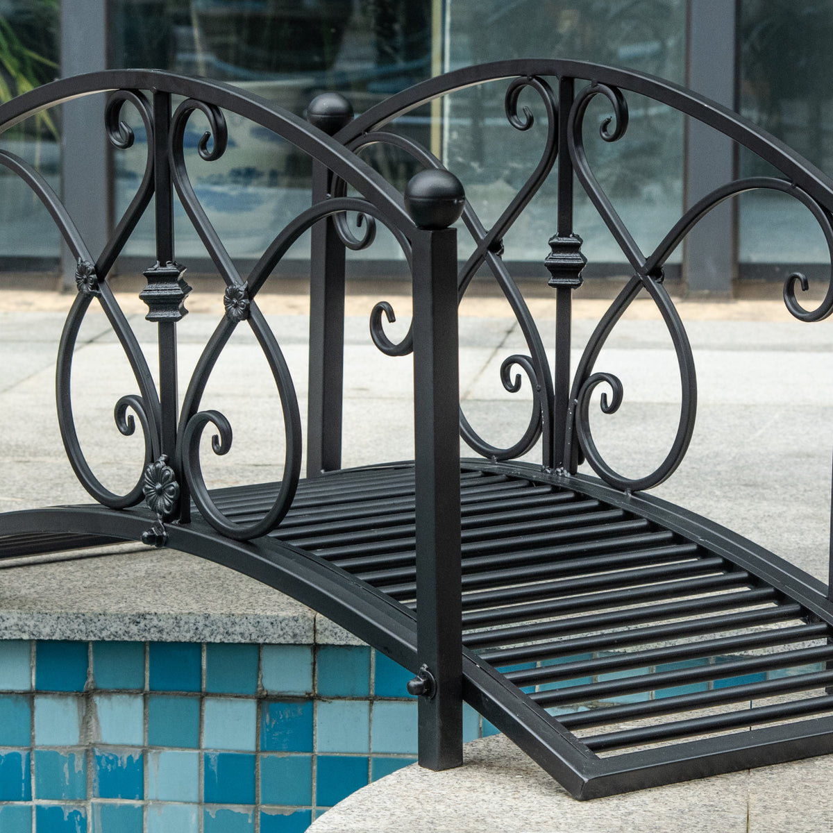 Arched black metal bridge showing decorative scrollwork railings and slatted deck