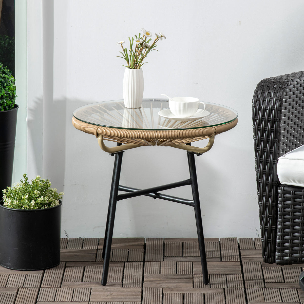 Beige woven side table with round glass top and black metal legs beside a patio chair