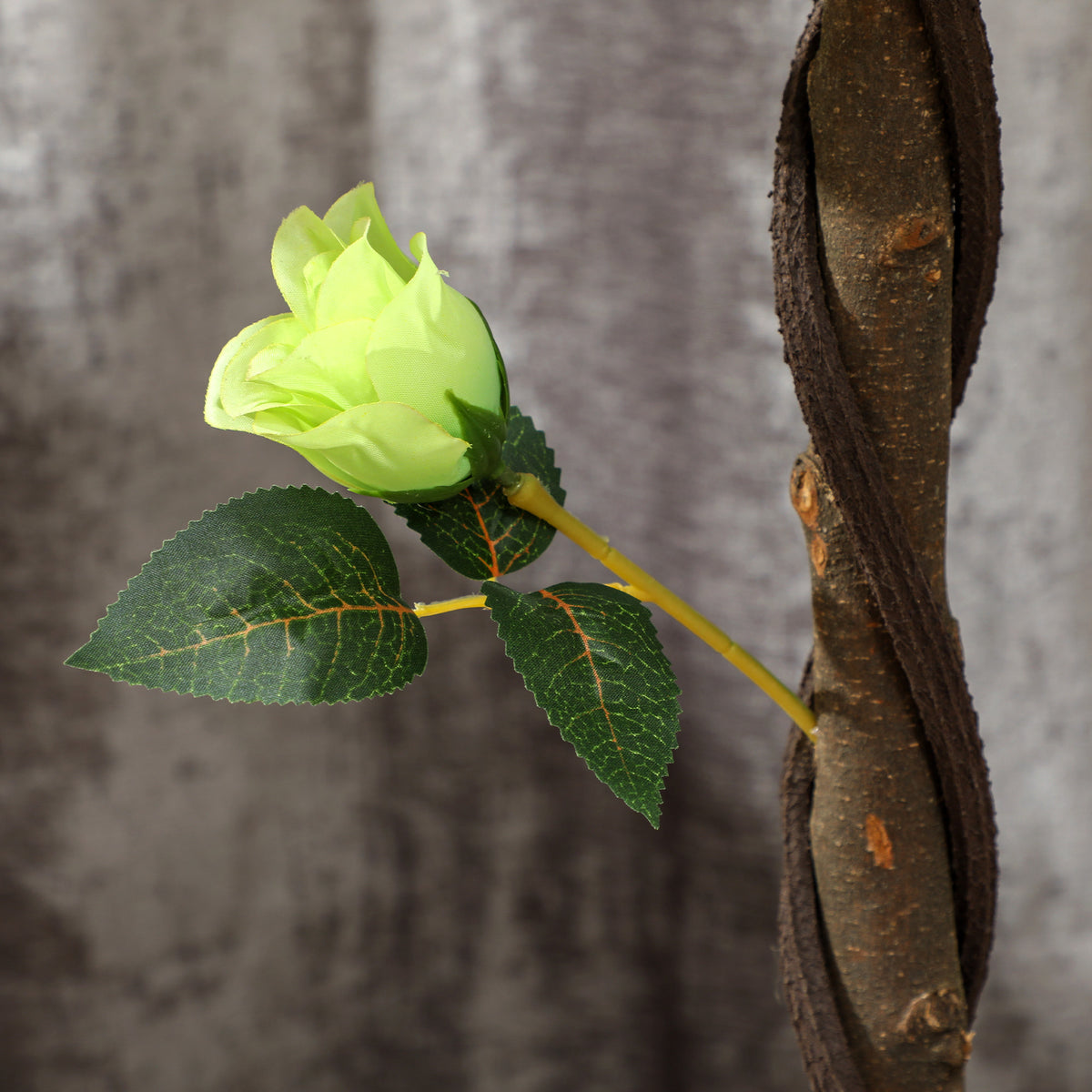 Faux rosebud and leaves on a branch beside the tree's textured trunk