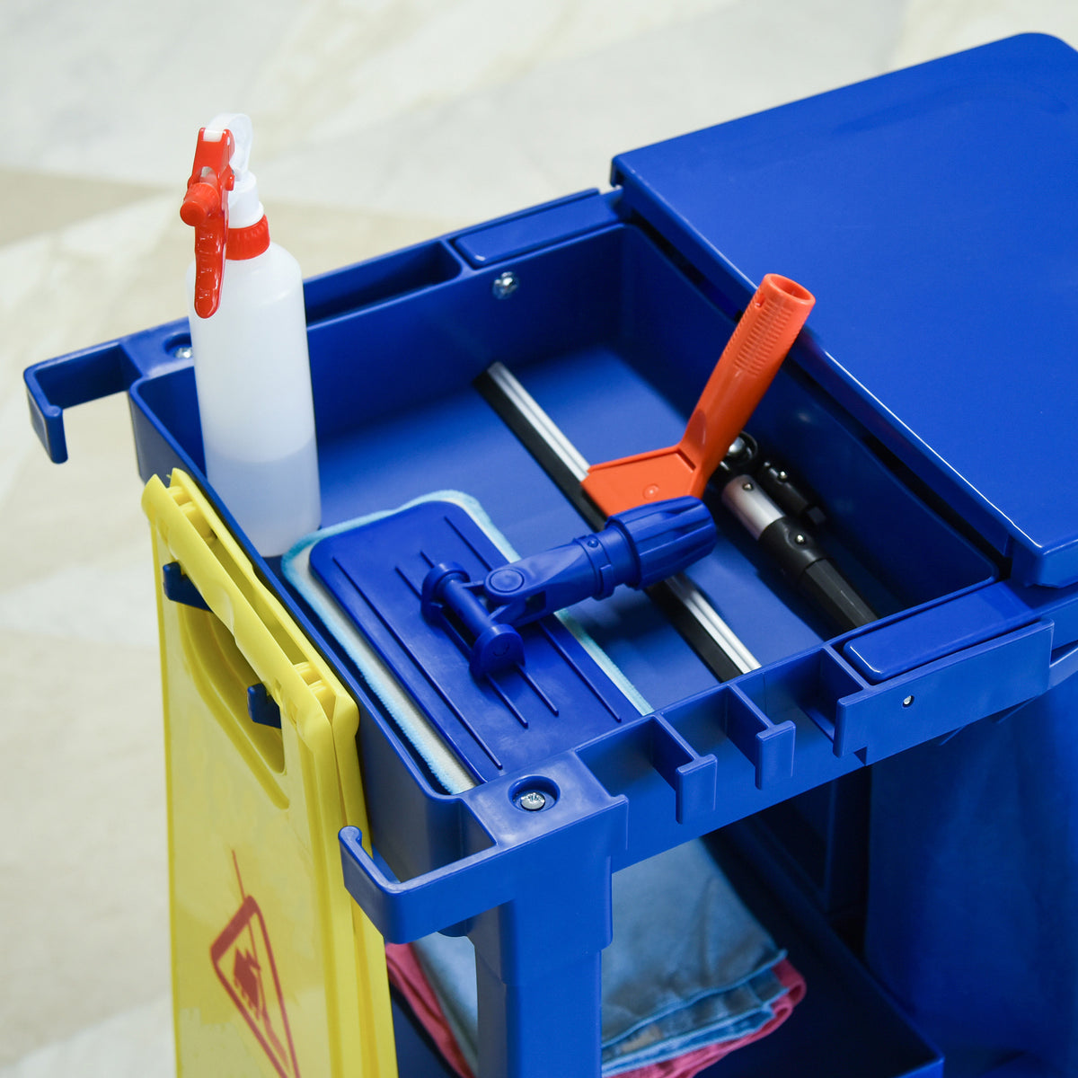 Blue cleaning trolley top compartments hold a spray bottle, mop tools and cloths.