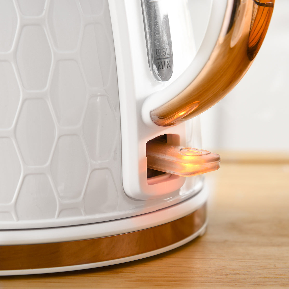 Close-up of white kettle's rose-gold handle, illuminated power switch and water gauge