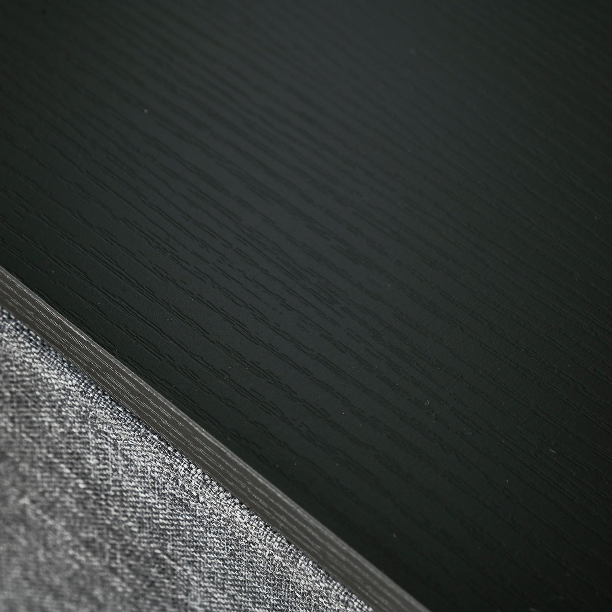 Close-up of the dresser's black wood-look top beside grey fabric