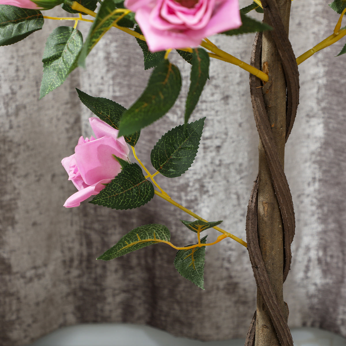 Close-up of an artificial rose tree's pink bloom, green leaves, and twisted brown trunk