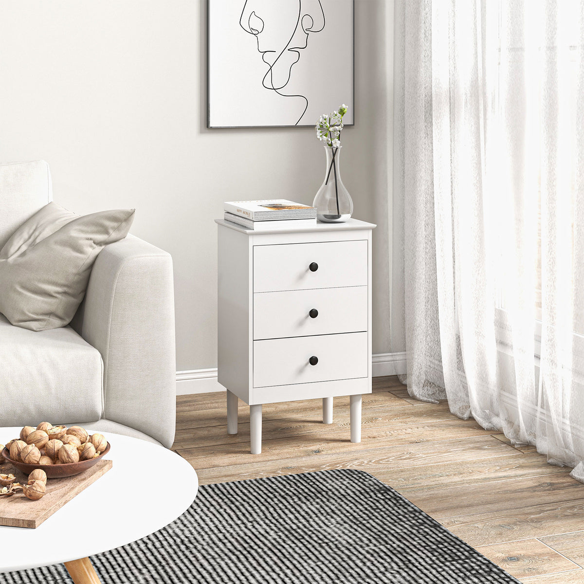 White three-drawer bedside table beside a sofa