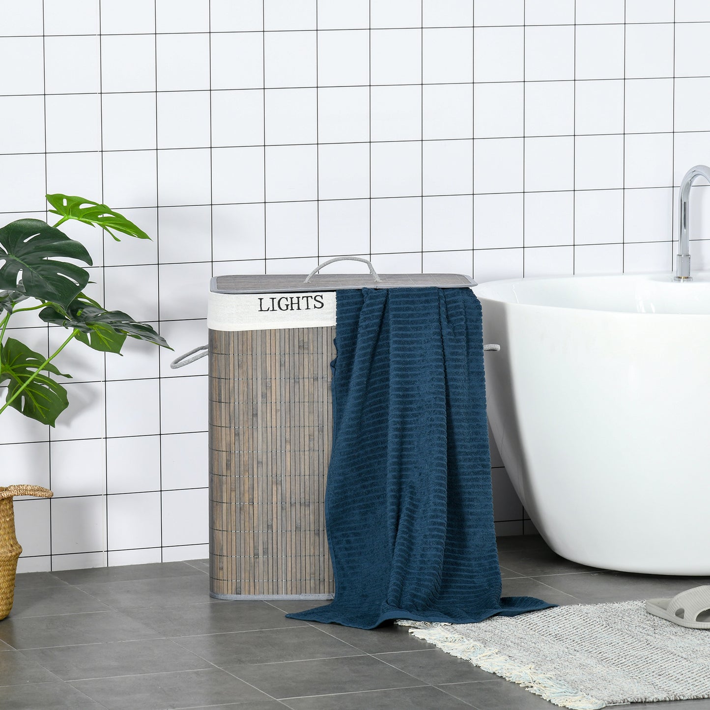 Gray two-section laundry hamper with lid and side handles beside a draped towel