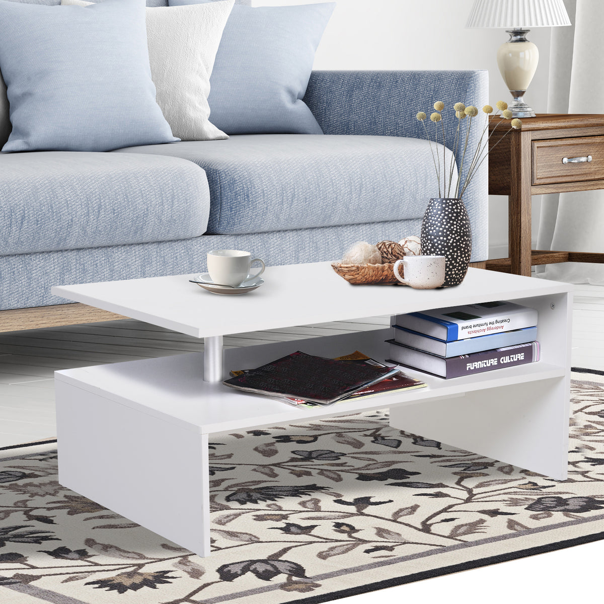White two-tier coffee table with cups and decor on top and books on its open shelf
