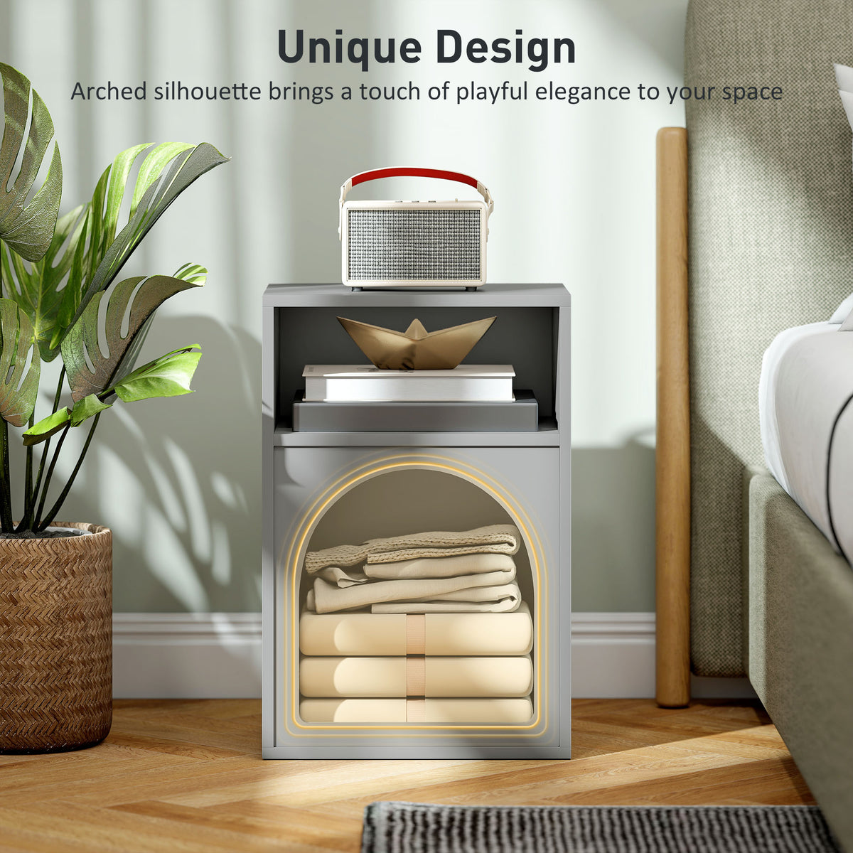 Grey bedside table with arched lower compartment holding folded linens