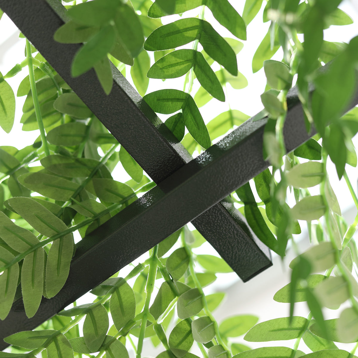 Close-up of intersecting dark metal trellis bars among climbing leaves
