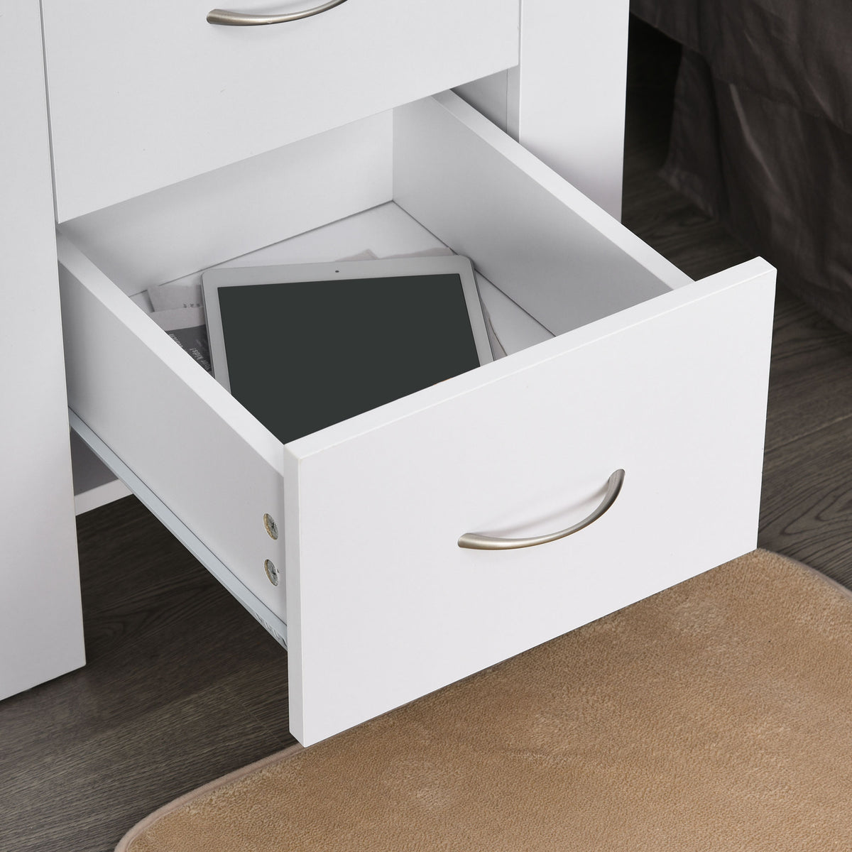Open drawer of a white bedside table showing its storage space and metal handle.