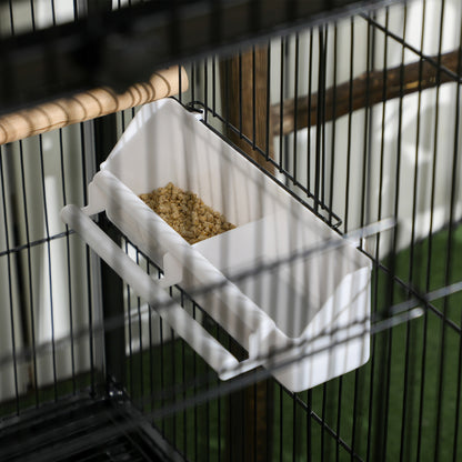 White hanging bird feeder filled with seed inside a black wire cage.