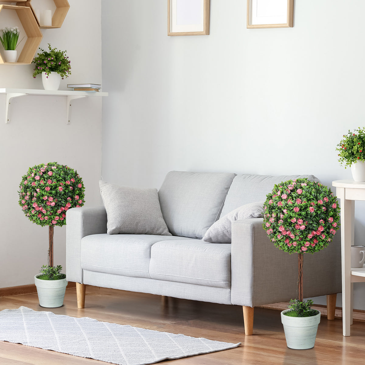 Two artificial rose topiary trees in white pots beside a living room sofa