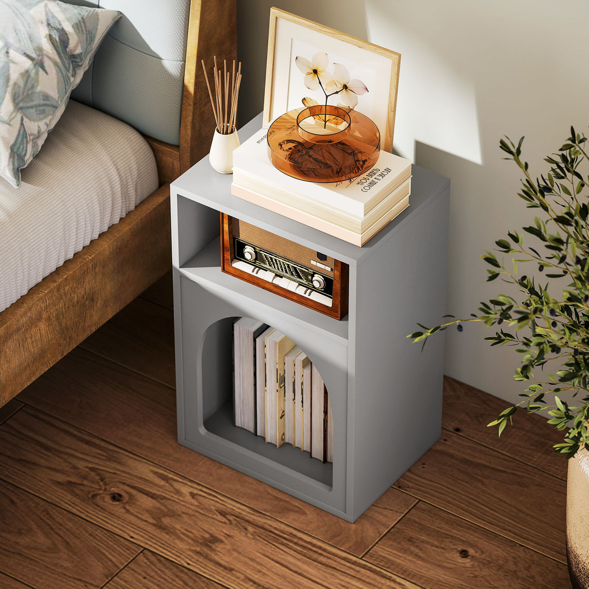 Grey bedside table with two open compartments, shown beside a bed