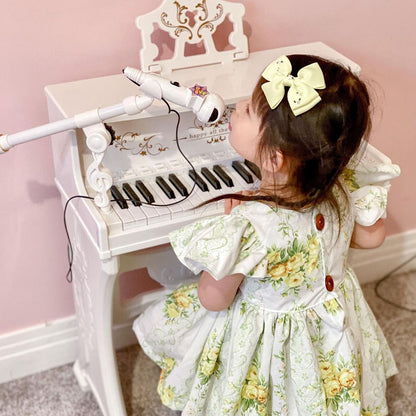 White toy piano with microphone and ornate stand, shown being played by a child.