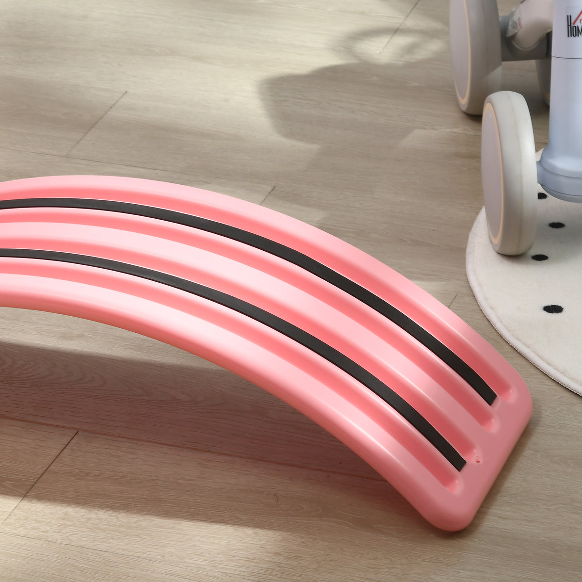 Pink children's balance board with two black anti-slip strips along its curved underside.