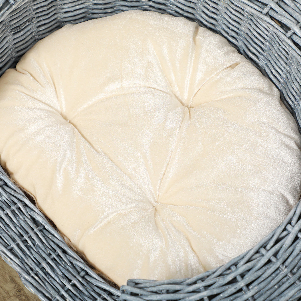 Close-up of a tufted cream cushion inside a gray wicker pet bed
