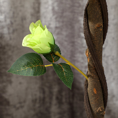 Faux rosebud and leaves on a branch beside the tree's textured trunk