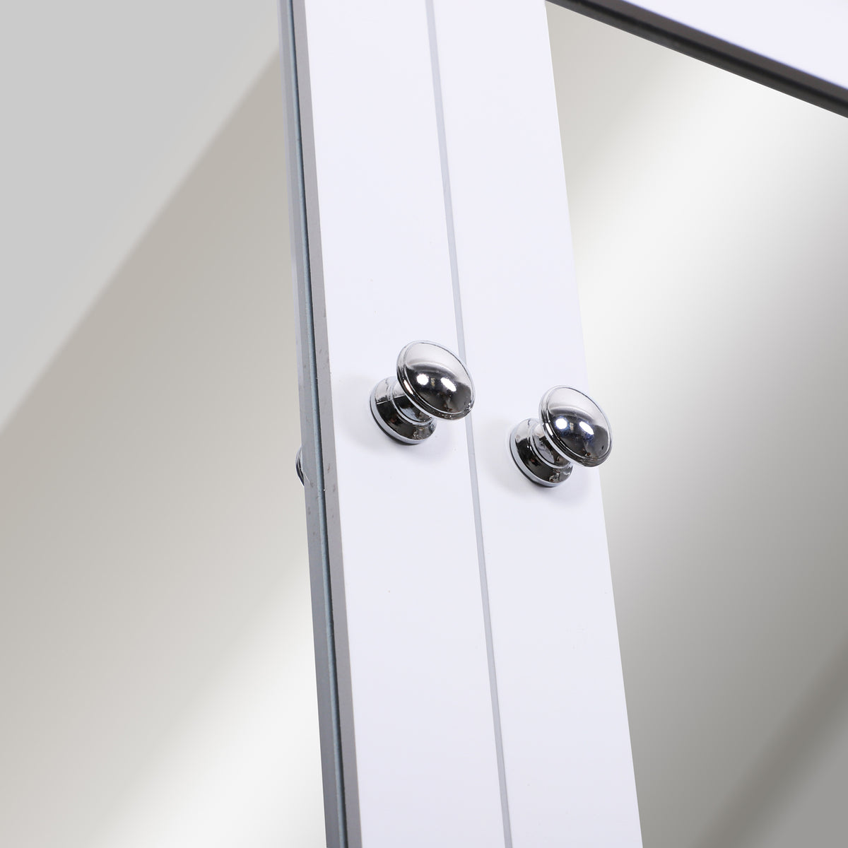 Close-up of chrome knobs on the white mirrored cabinet doors