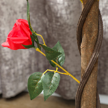Close-up of an artificial red rose, green leaves and textured twisted trunk