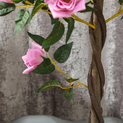 Close-up of an artificial rose tree's pink bloom, green leaves, and twisted brown trunk