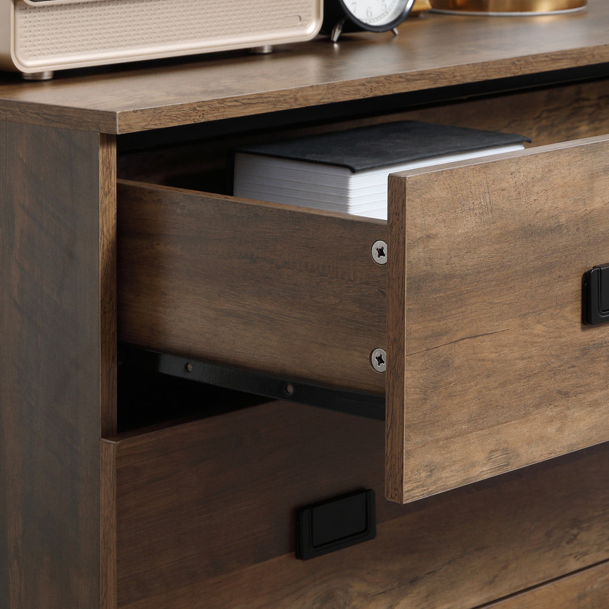 Close-up of an open brown chest drawer with a black handle and metal slide