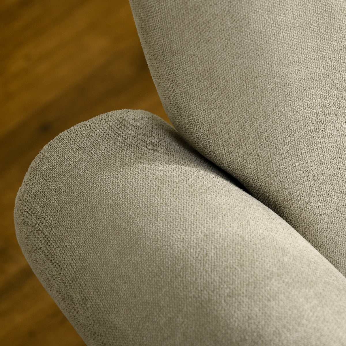 Close-up of the chair's beige textured upholstery and rounded arm.
