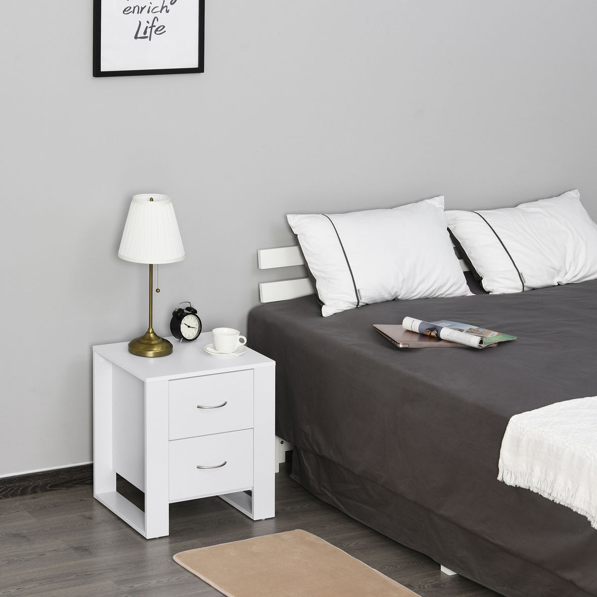 White two-drawer bedside table beside a bed, topped with a lamp and small decor.